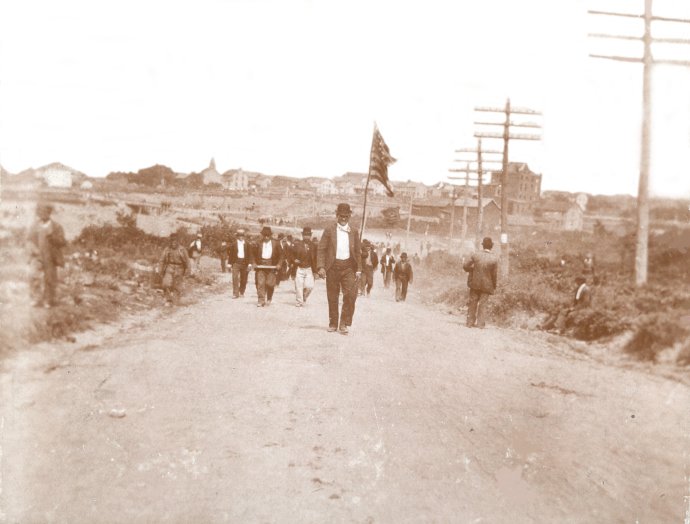 Jedna z mála fotiek z masakry. Baníci pochodujúci do Lattimera si vzali so sebou aj americkú zástavu, ktorú niesol Slovák Steve Jurich. Zdroj – Pennsylvania State Archives