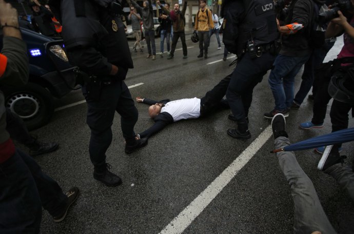 Poriadková polícia ťahá po zemi ležiaceho demonštranta pred volebnou miestnosťou v Barcelone počas referenda o nezávislosti Katalánska. Foto - TASR/AP