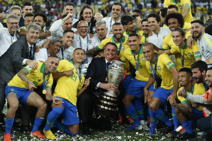 Brazílsky prezident Bolsonaro drží trofej za víťazstvo na Copa América a oslavuje s hráčmi. Foto – AP/Victor R. Caivano