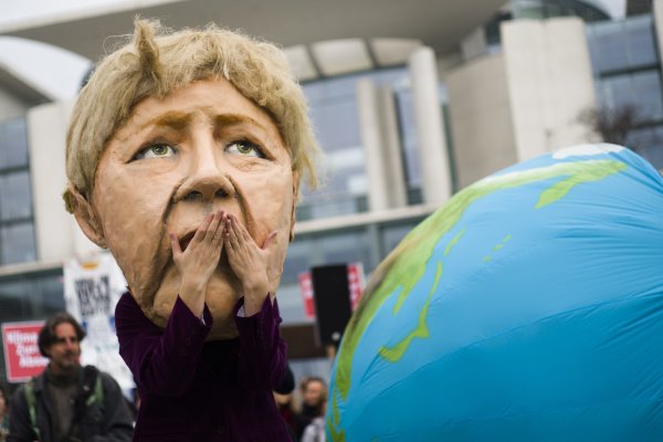 Demonštrant v maske nemeckej kancelárky Angely Merkelovej protestuje proti balíku prijatých klimatických opatrení nemeckej vlády. Foto - TASR/AP