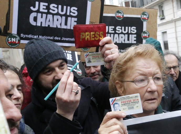 Novinári ukazujú svoje preukazy a ceruzku počas minúty ticha za obete pred sídlom týždenníka Charlie Hebdo. Foto - TASR/AP