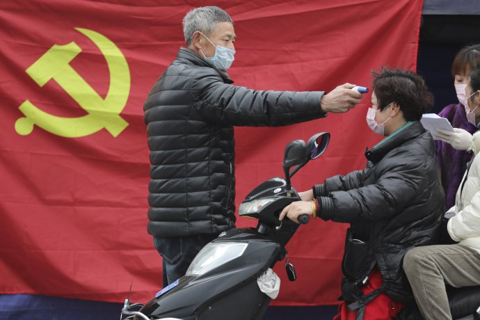 Dobrovoľník meria vodičovi skútra teplotu pred vlajkou čínskej komunistickej strany. Foto - TASR/AP