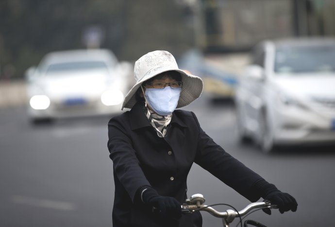 Žena na bicykli s rúškom na tvári v Pekingu 22. októbra 2013. Foto – TASR/AP