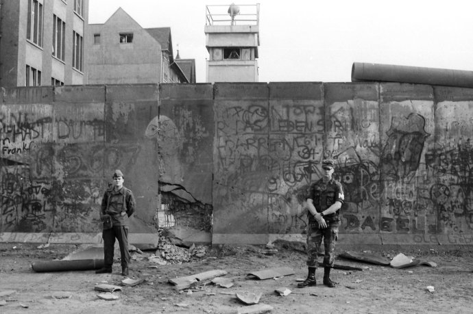 Na archívnej snímke z 28. júla 1986 pohraničný vojak Nemeckej demokratickej republiky (NDR) a americký vojak strážia Berlínsky múr pri kontrolnom bode Charlie na ulici Charlottenstrasse. Foto - TASR/AP