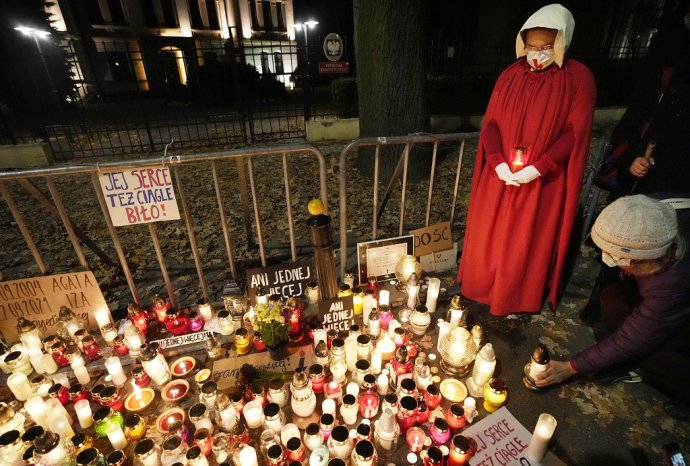 Poľky a Poliaci zapaľujú sviečky na pamiatku Izabely, ktorá zomrela v 22. týždni tehotenstva. Žena na fotke je oblečená ako postavy zo seriálu The Handmaid's Tale, v ktorom plodné ženy nútili vynosiť deti neplodných párov. Foto - TASR/AP