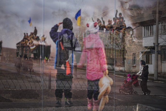 Dvojica s kočíkom prechádza okolo veľkej fotografie venovanej pamiatke ľudí zabitých počas vojny na Donbase. Foto - TASR/AP