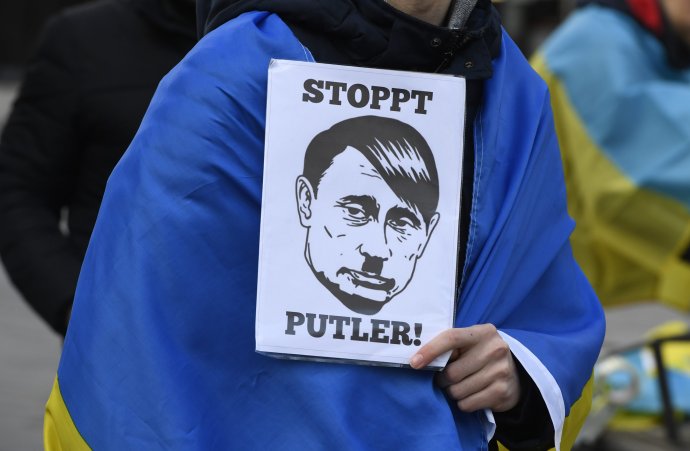 Demonštrant v nemeckom Düsseldorfe zahalený v ukrajinskej vlajke drží transparent s nápisom "Zastavte Putlera". Foto - TASR/AP
