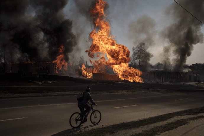 Muž na bicykli prechádza okolo veľkého požiaru po ruskom útoku v Charkive. Foto - TASR/AP