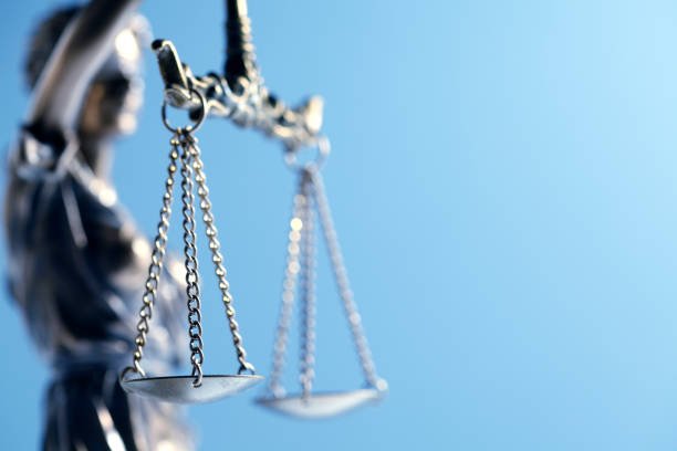 A close up and a low angle view of a statue of lady justice as it sits in front of a blue background The image is photographed with a very shallow depth of field with the focus being on the justice scale.