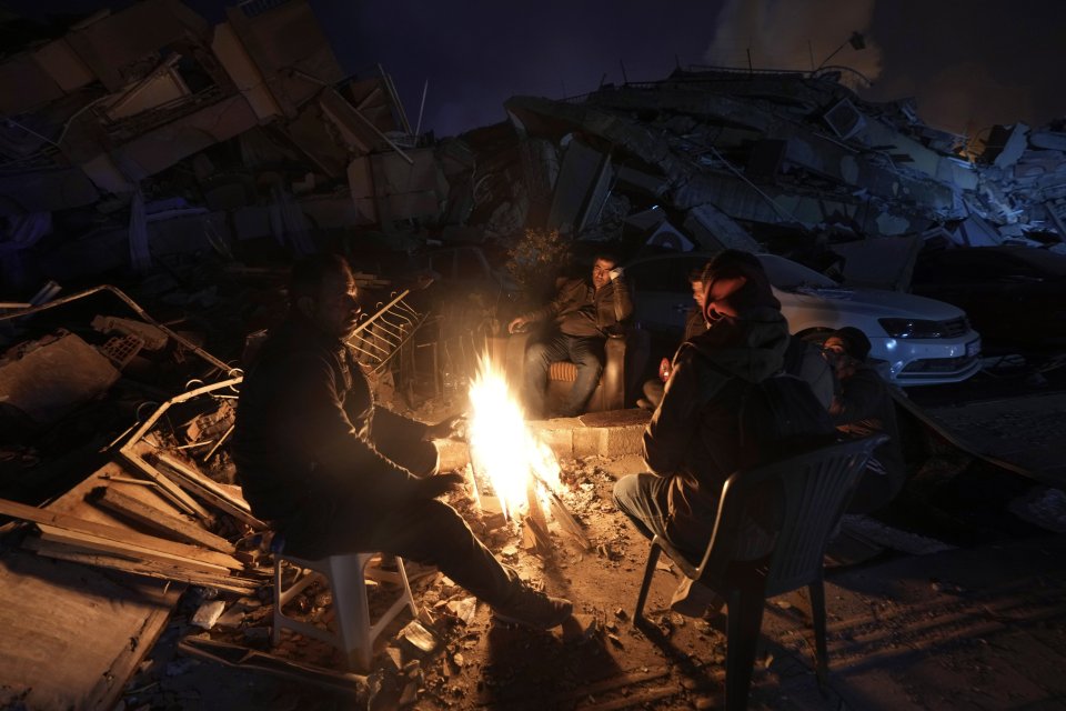 Ľudia sa zohrievajú pri ohni medzi zničenými budovami v Antakyi na juhu Turecka. Foto - tasr/ap