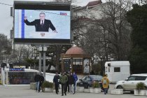 People walk in front of a tv screen showing Russian President Vladimir Putin during his annual state of the nation address in in Sevastopol, Crimea, Tuesday, Feb. 21, 2023. (AP Photo)